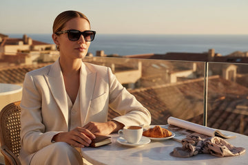 Woman in DG sunglasses and a white jacket sitting at a table