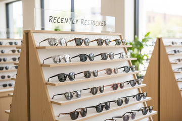Display of sunglasses on wooden shelves with 'Recently Restocked' sign in the background.